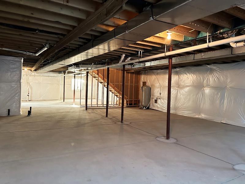 An empty basement with a staircase and a lot of pipes.