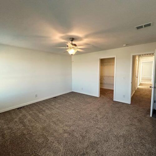 An empty bedroom with a ceiling fan and a walk in closet.