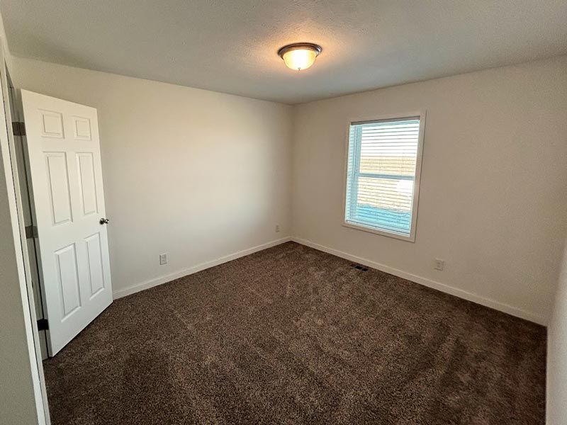 An empty bedroom with a window and a brown carpet.