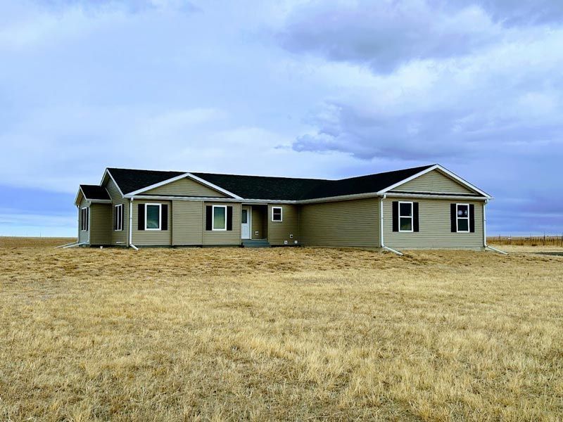 A house in the middle of a field with a cloudy sky in the background