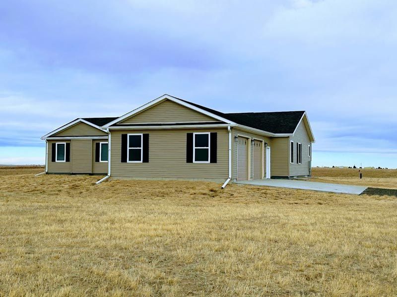 A house with black shutters is in the middle of a field