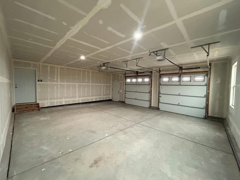 An empty garage with two garage doors and a ceiling fan.