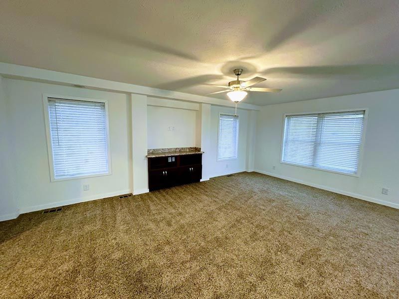 An empty living room with a ceiling fan and lots of windows.