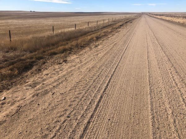 A dirt road in the middle of a field with a fence in the background.