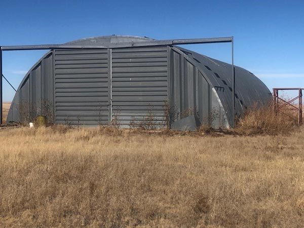 A large metal building is sitting in the middle of a dry grass field.