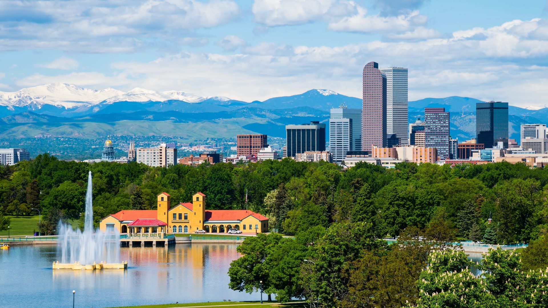 A fountain in a park in front of a city skyline with mountains in the background.