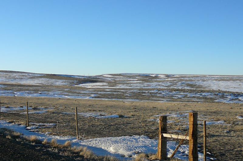 A wooden fence surrounds a snowy field with a blue sky in the background.