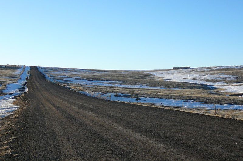 A dirt road going through a snowy field.