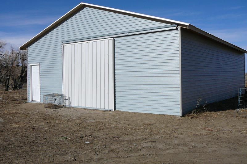 A large white barn with a sliding door is in the middle of a dirt field.