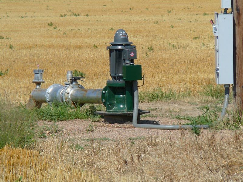 A green pump is sitting in the middle of a field