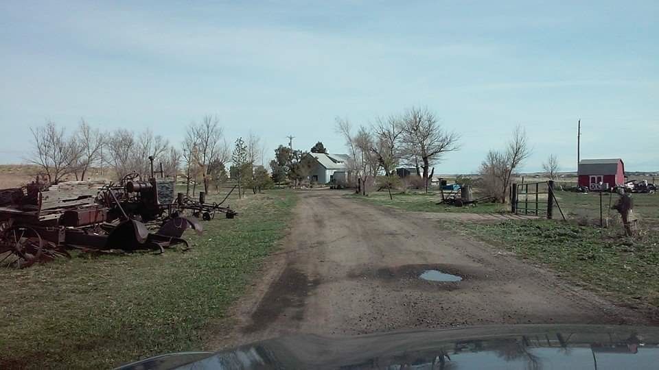 A dirt road leading to a farm with a red barn in the background.