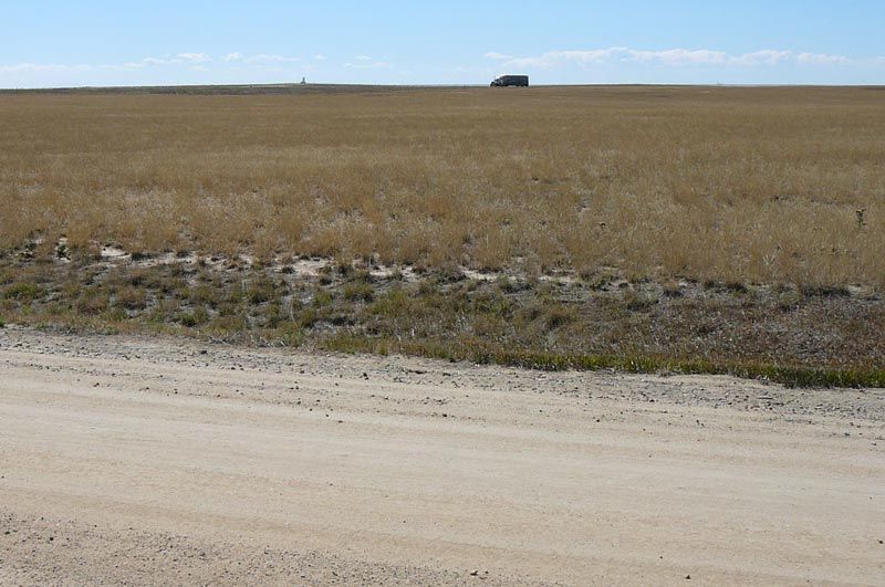 A dirt road going through a field with a truck in the distance.