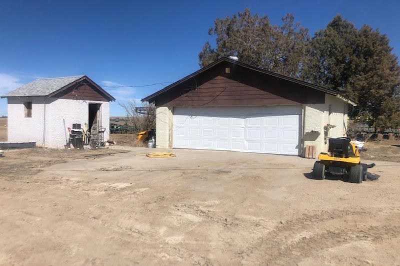 A yellow lawn mower is parked in front of a garage.