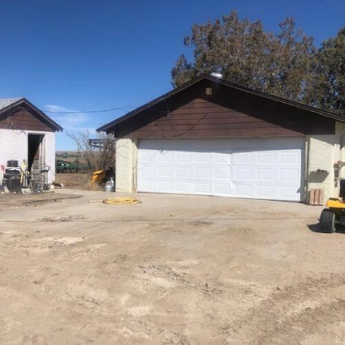 A yellow tractor is parked in front of a garage door.