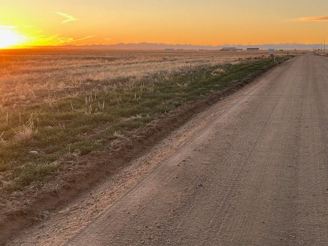 Dirt road through a field at sunrise with a golden sky and distant mountains.