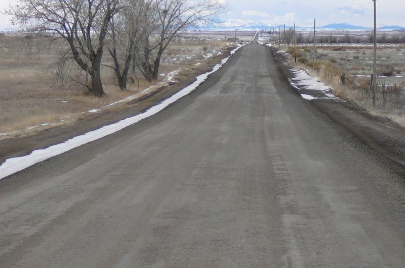 A road with snow on the side of it and trees on the side.