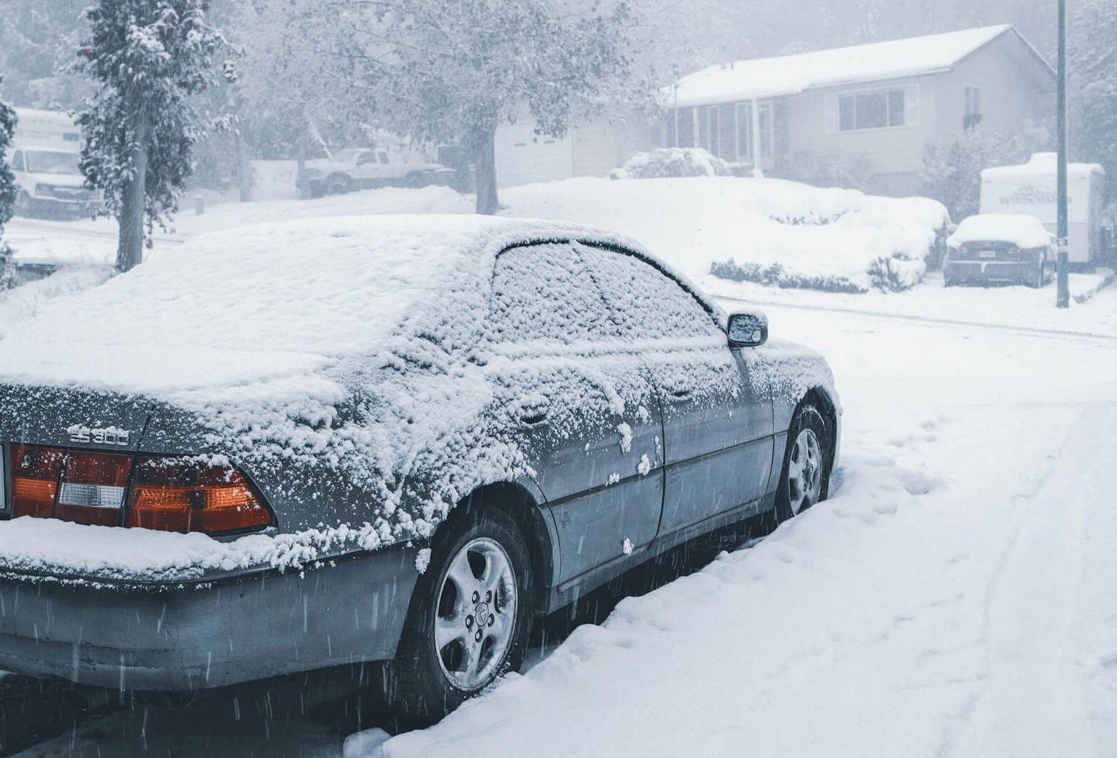 Sedan car in a neighborhood driveway, covered in snow in extreme cold