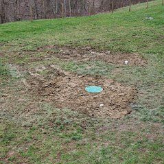 There is a hole in the ground in the middle of a grassy field.