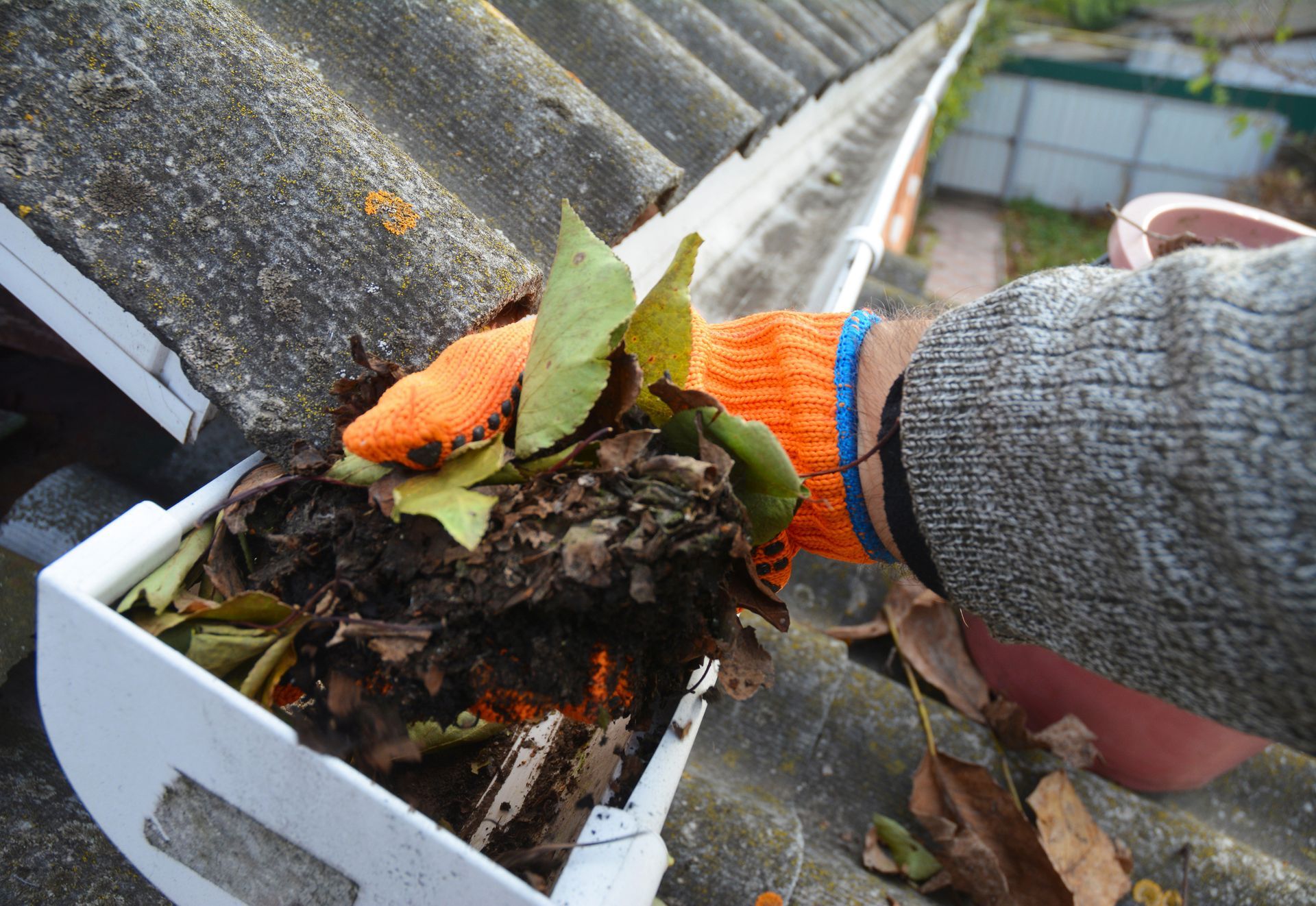 Person wearing orange glove cleans out clogged gutter of leaves.
