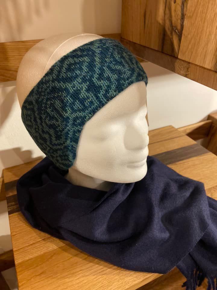 Eine Schaufensterpuppe mit Stirnband und Schal sitzt auf einem Holztisch.