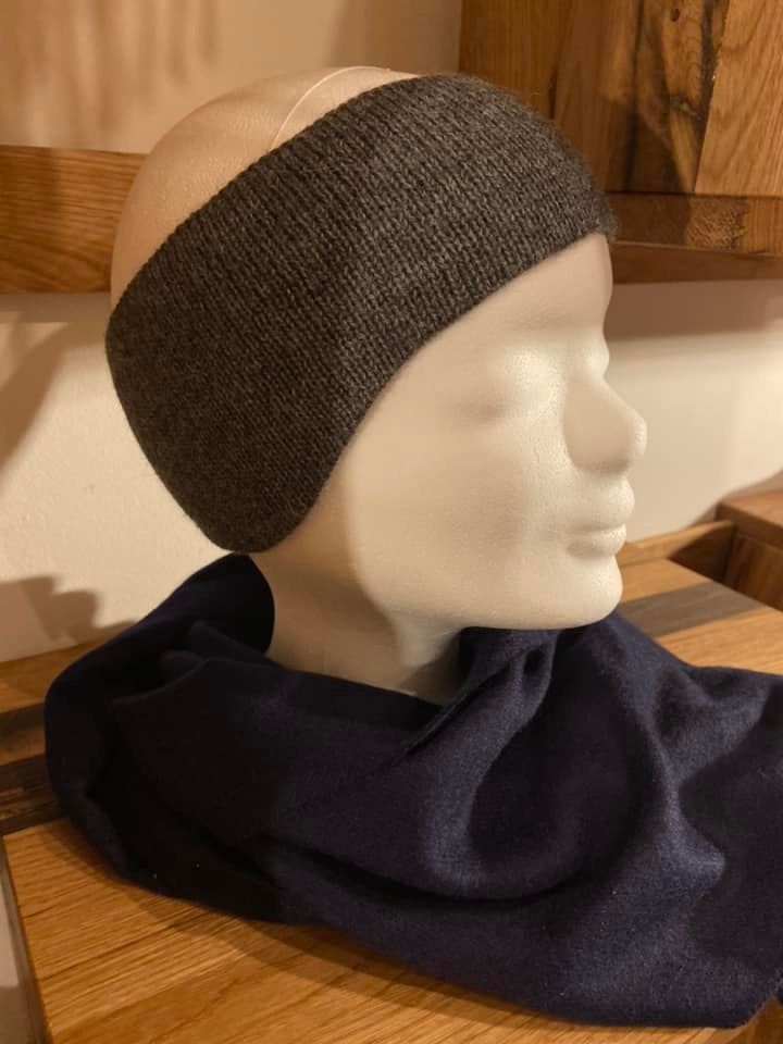 Eine Schaufensterpuppe mit Stirnband und Schal sitzt auf einem Holztisch.