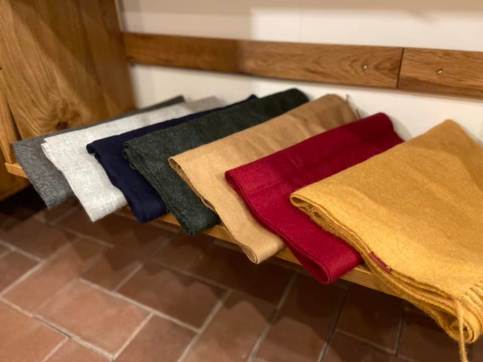 Eine Reihe von Schals liegt aufgereiht auf einem Holzregal.