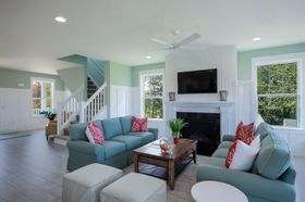 Spacious living room with turquoise sofas, fireplace, and staircase. Green walls, white trim, and light wood floors.