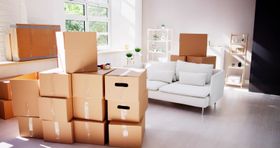 Boxes stacked in a room with a white sofa and sunlight streaming through a window.