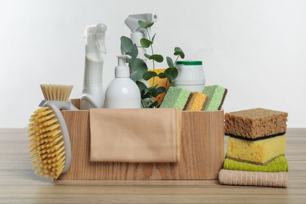 Wooden box with cleaning supplies: brushes, spray bottles, sponges, and towels.