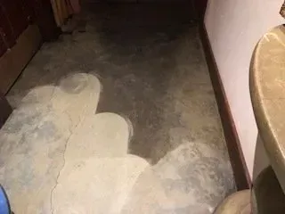 Partially sanded hallway floor with bare concrete and a lighter patch near the wall
