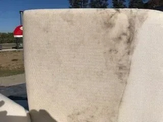Dirty white upholstered chair with dark stains and wear outdoors