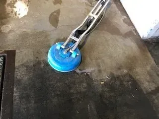 Blue floor-cleaning machine on a wet concrete floor near a wall