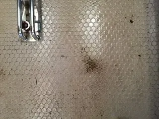 Close-up of a light gray textured surface with a metal latch at the top left and a small dark stain near center