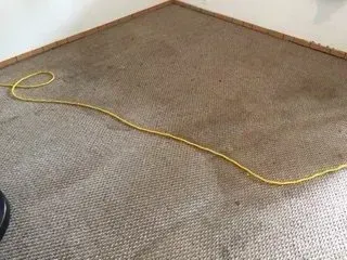 Yellow extension cord lying across a beige carpet in a corner of a room.