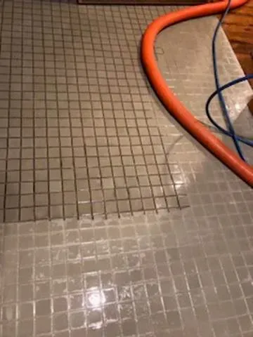 Wet tiled floor with a square-gridded surface and an orange hose along the edge