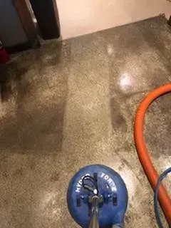 Blue floor-cleaning machine on a wet concrete floor with an orange hose attached.