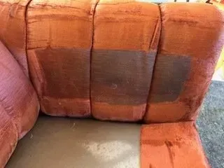 Orange-brown striped sofa with a worn seat and dark stains on the cushions
