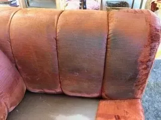 Close-up of a worn salmon-colored upholstered couch with three back cushions and a gray seat.