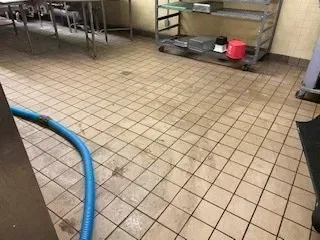 Commercial kitchen floor with a blue hose, metal shelves, and tiled flooring.