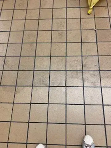 Tiled floor with two people’s shoes visible at the bottom edge and a yellow object in the upper right corner