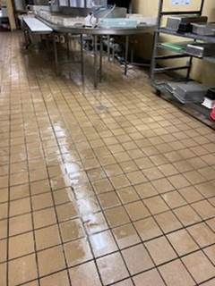 Commercial kitchen floor with a wet spill reflecting light under metal counters and shelving