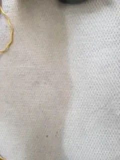 Close-up of a light beige textured fabric with a small yellow thread loop at the edge.