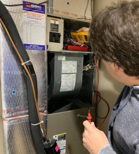 Person using a multimeter to inspect an HVAC unit, inside a home.
