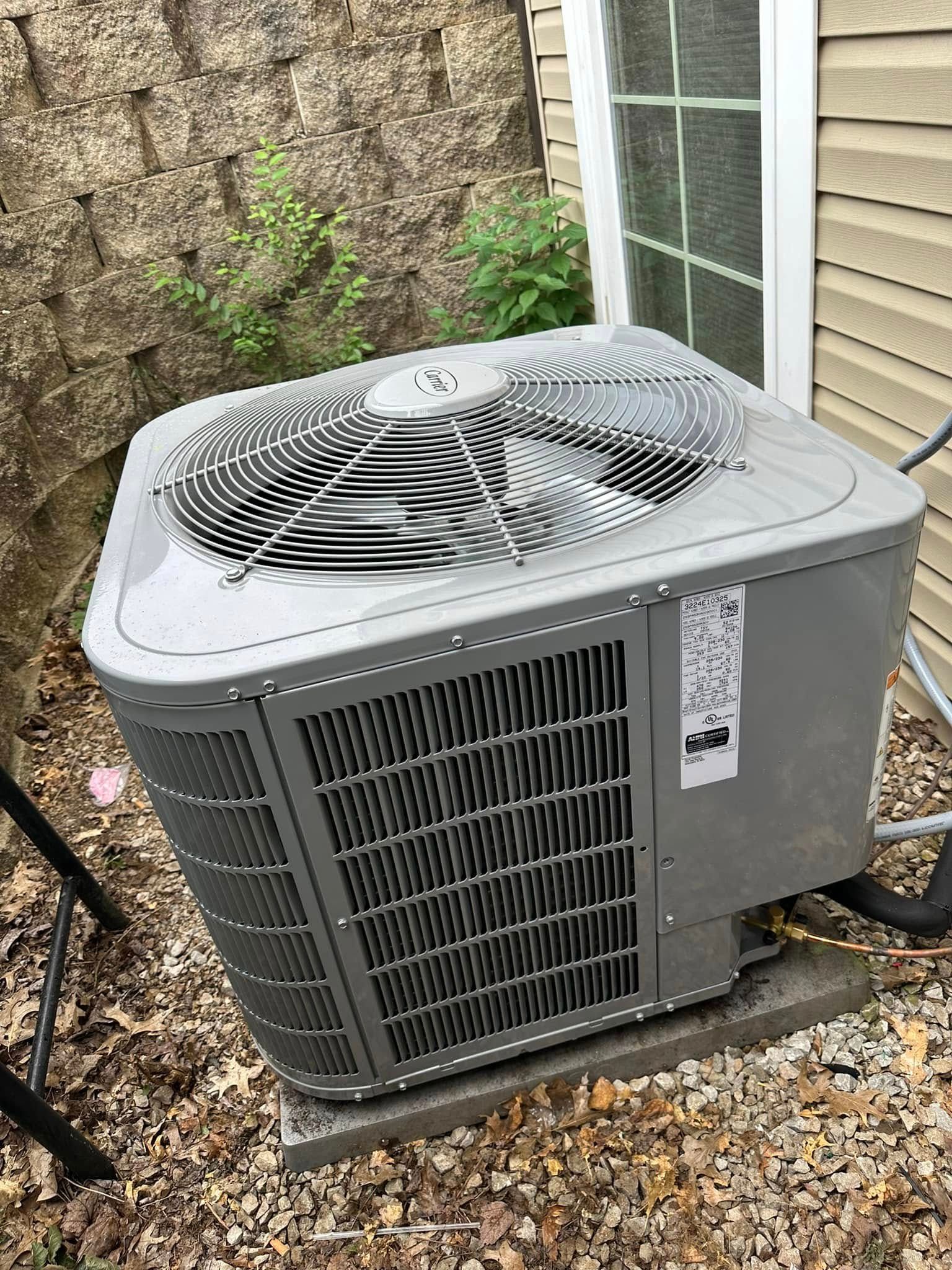 A person digs a trench in a backyard near a small excavator, a tree, and a house.
