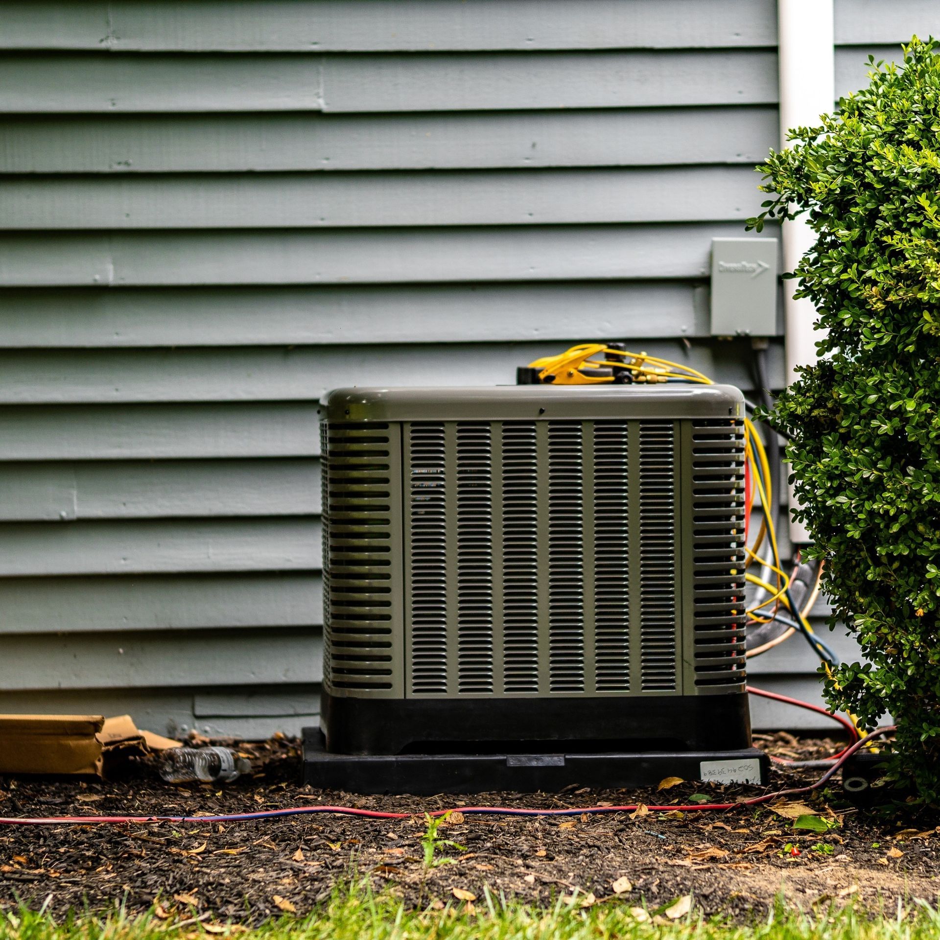 Air conditioning unit next to a house and bush.