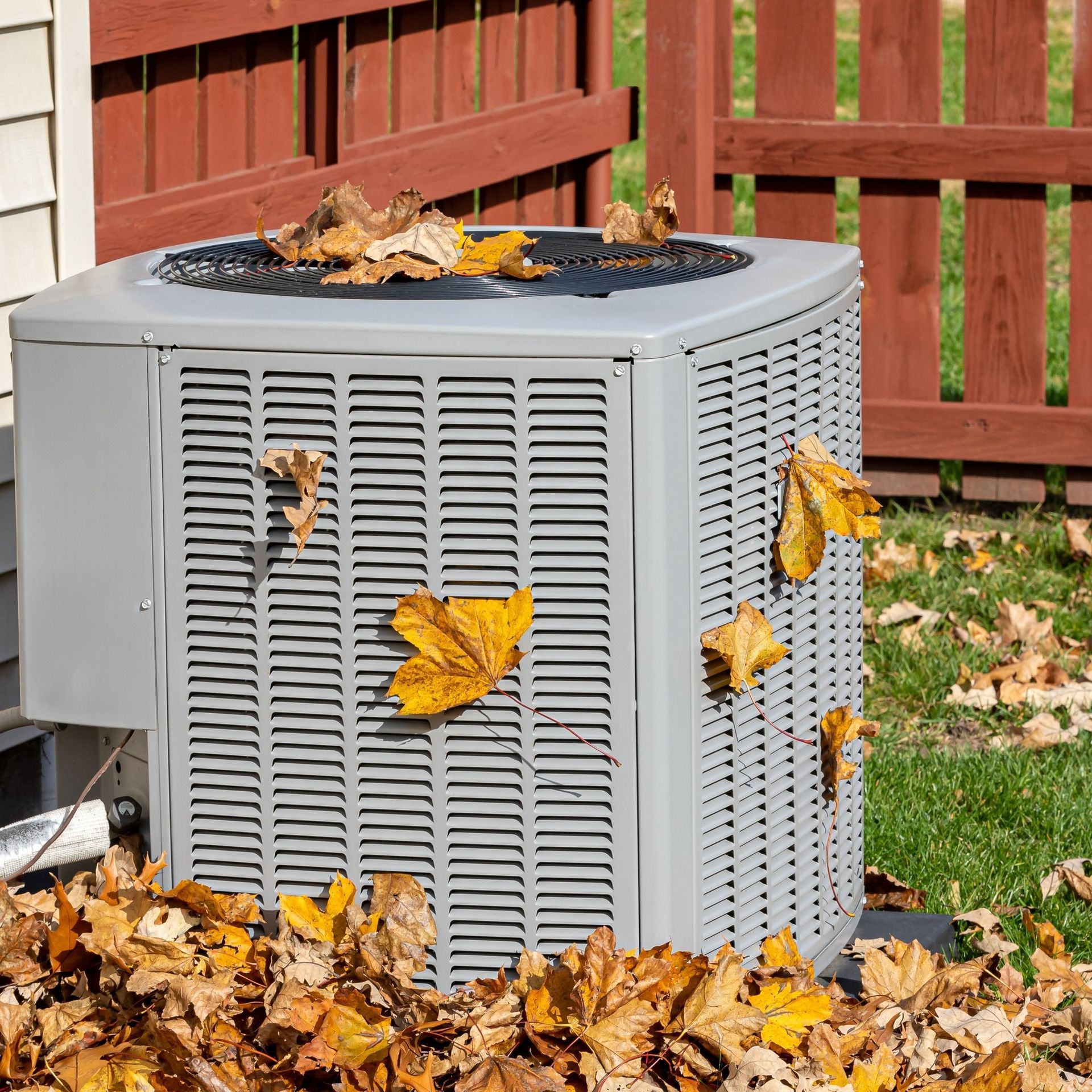 Air conditioning unit covered in fallen leaves, outdoors.