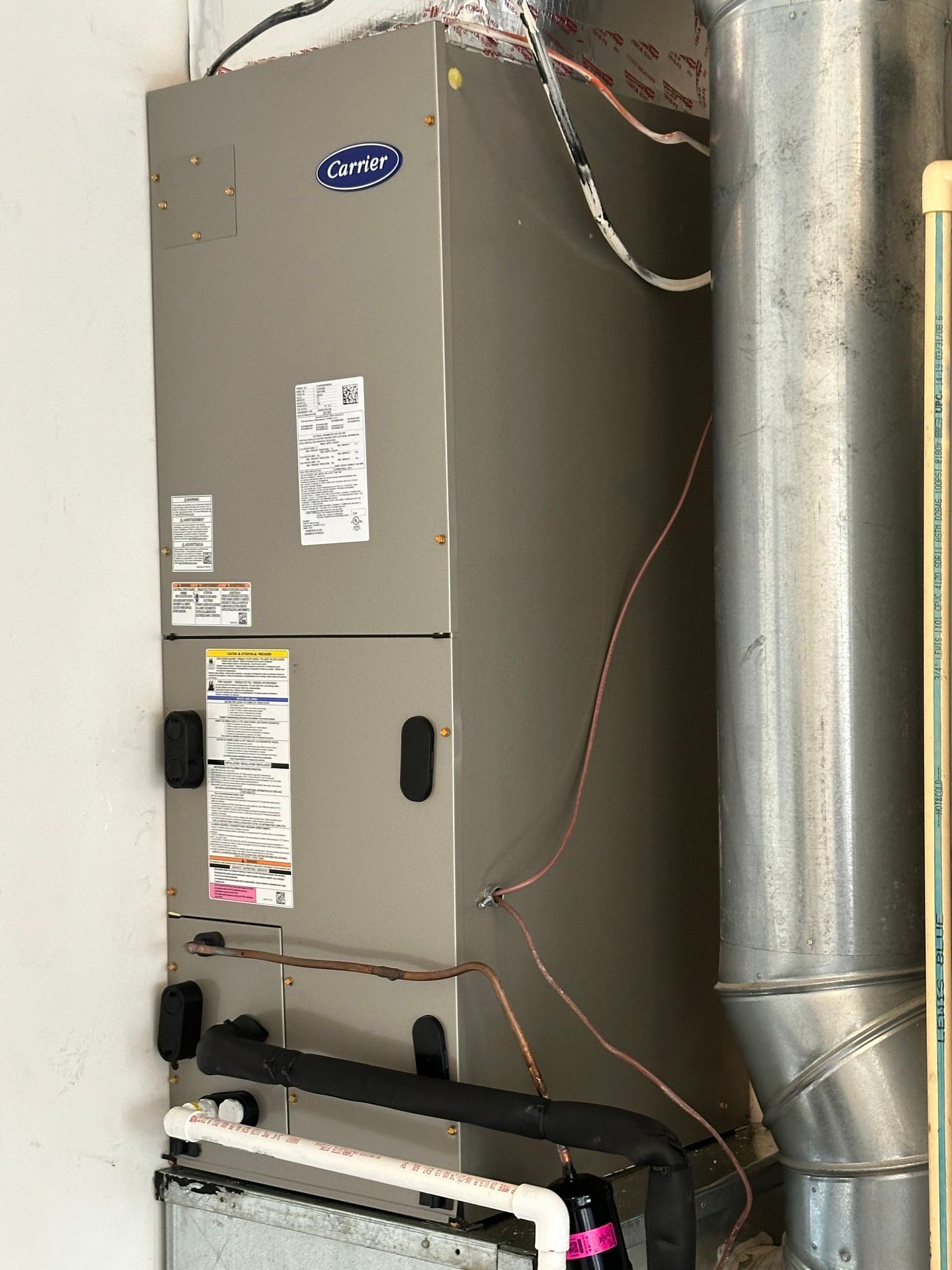 A tall, gray Carrier HVAC unit with exposed wiring and ductwork in a utility space.