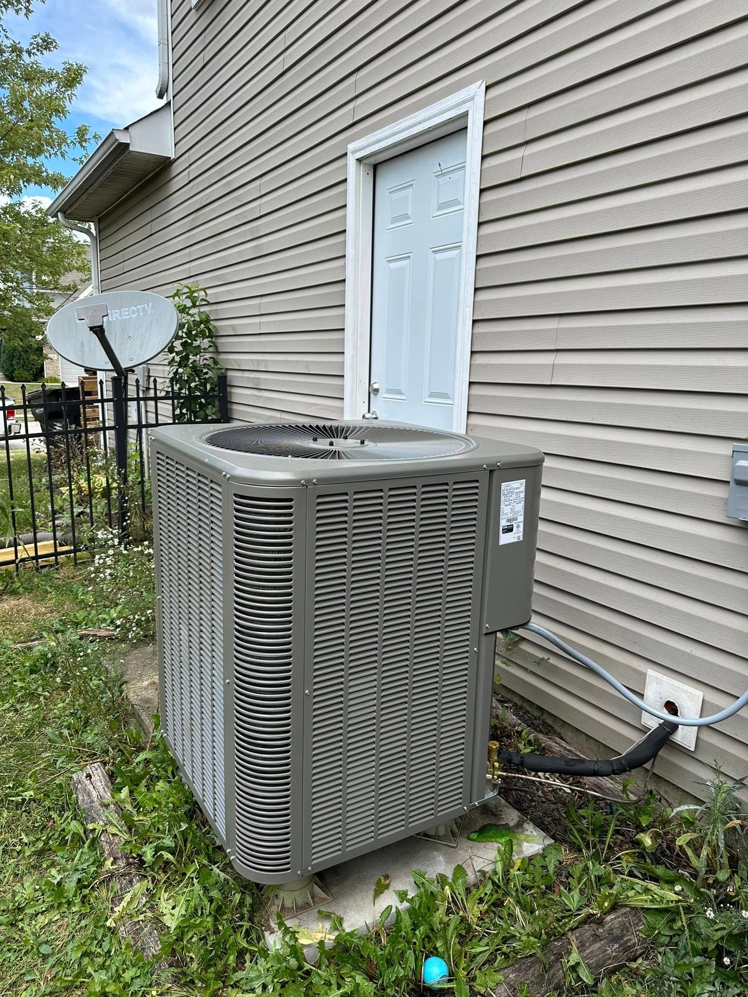 Air conditioning unit outside a building with a white door, set in grass.