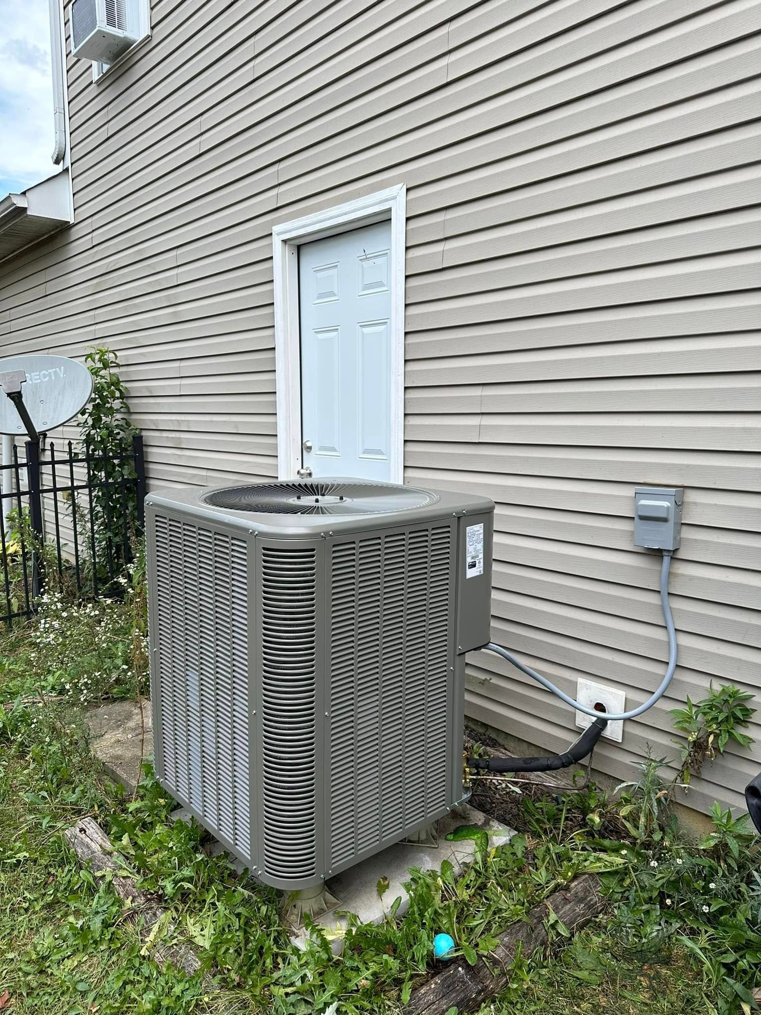 Trench dug in a grassy yard, leading to a house with black siding, and an electrical box.