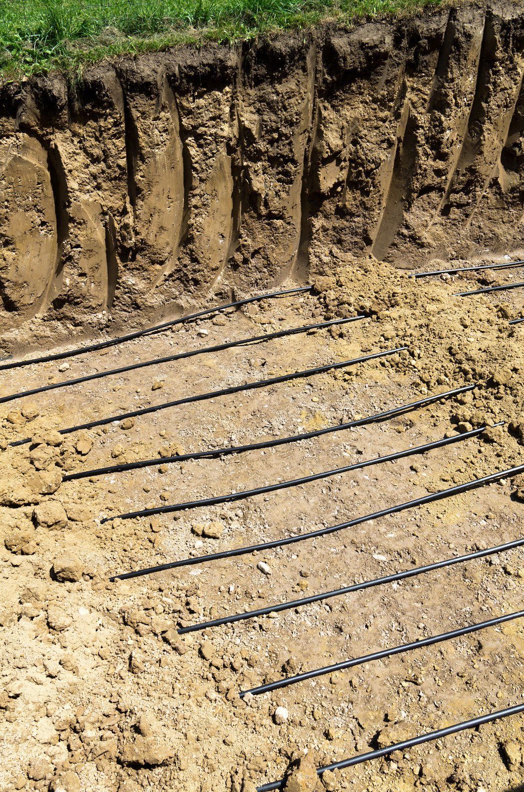Trench dug in a grassy yard, leading to a house with black siding, and an electrical box.